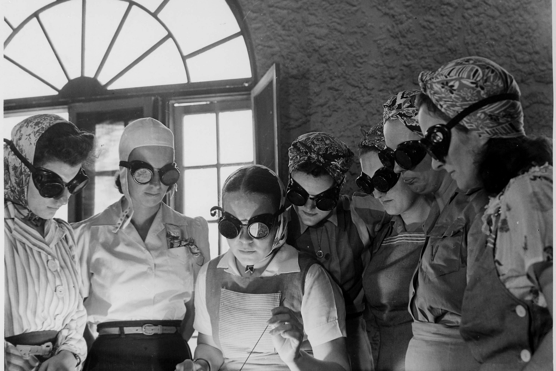 Image of several women with light-blocking goggles standing over bright World War 2-era machinery.